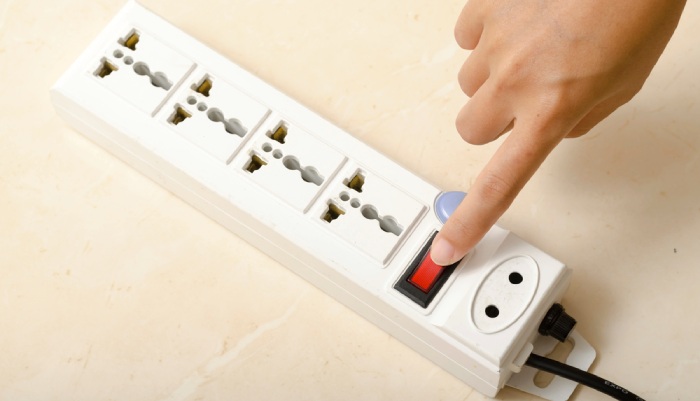 A hand turning on a switch button of multiple socket plug