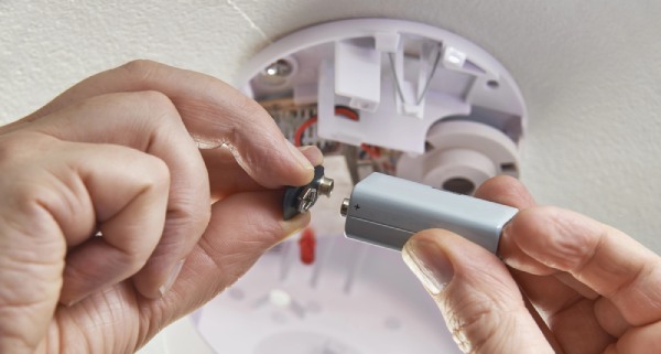 A person replacing smoke alarm batteries