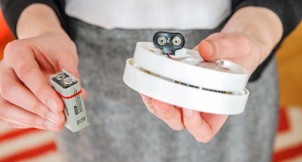 A person showing 9 volt batteries inside smoke alarm detector